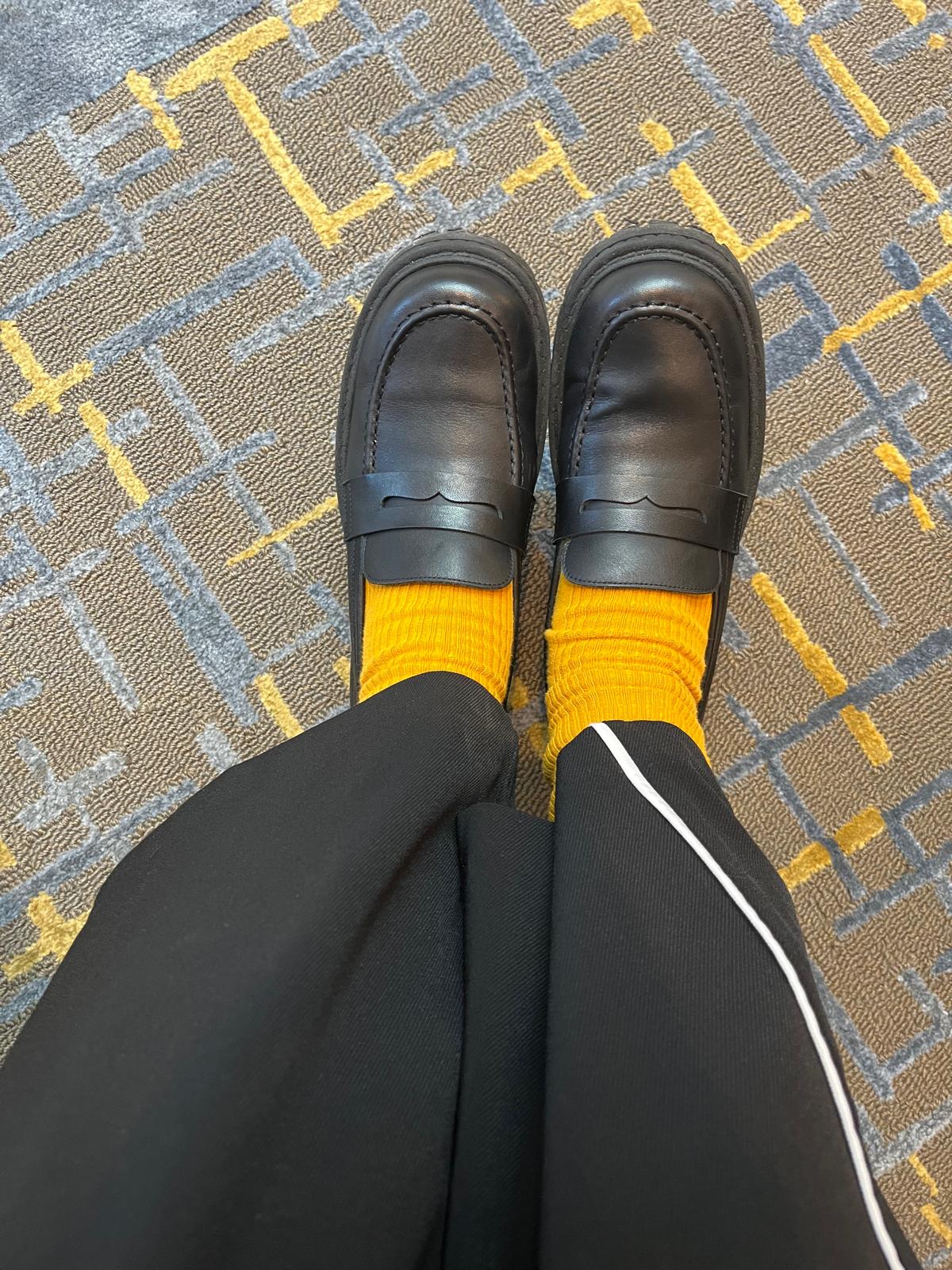Person wearing black loafers and yellow socks on a patterned carpet