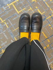 Person wearing black loafers and yellow socks on a patterned carpet