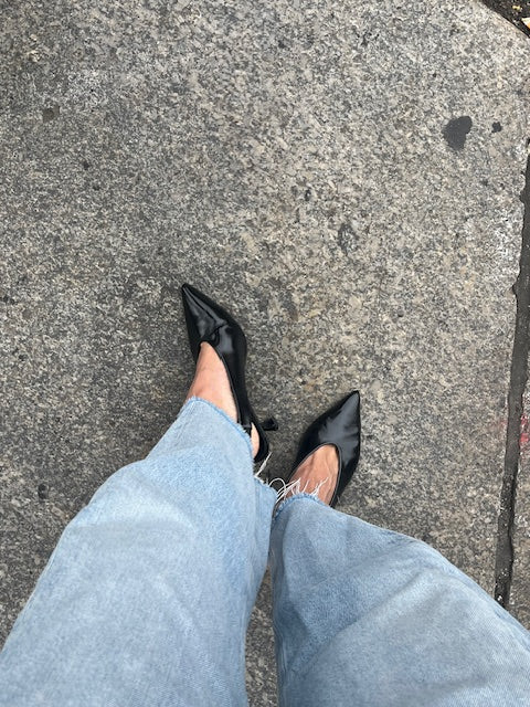 Woman wearing denim and black high-heeled slingback shoes on a gray pavement