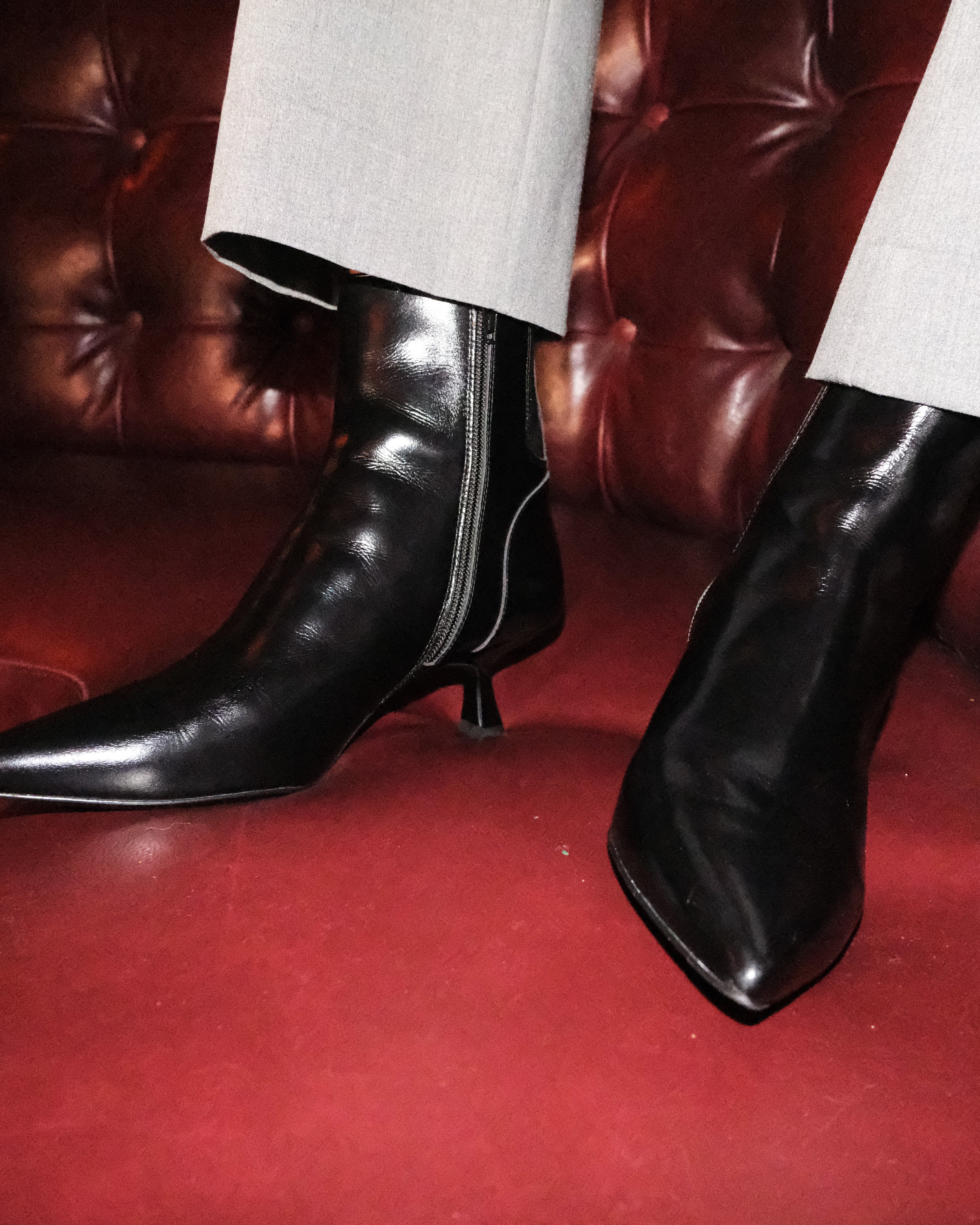 Black leather boots worn with gray pants on a red leather couch.