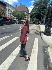 Woman standing on a city street corner holding a coffee cup wearing black slingbacks.