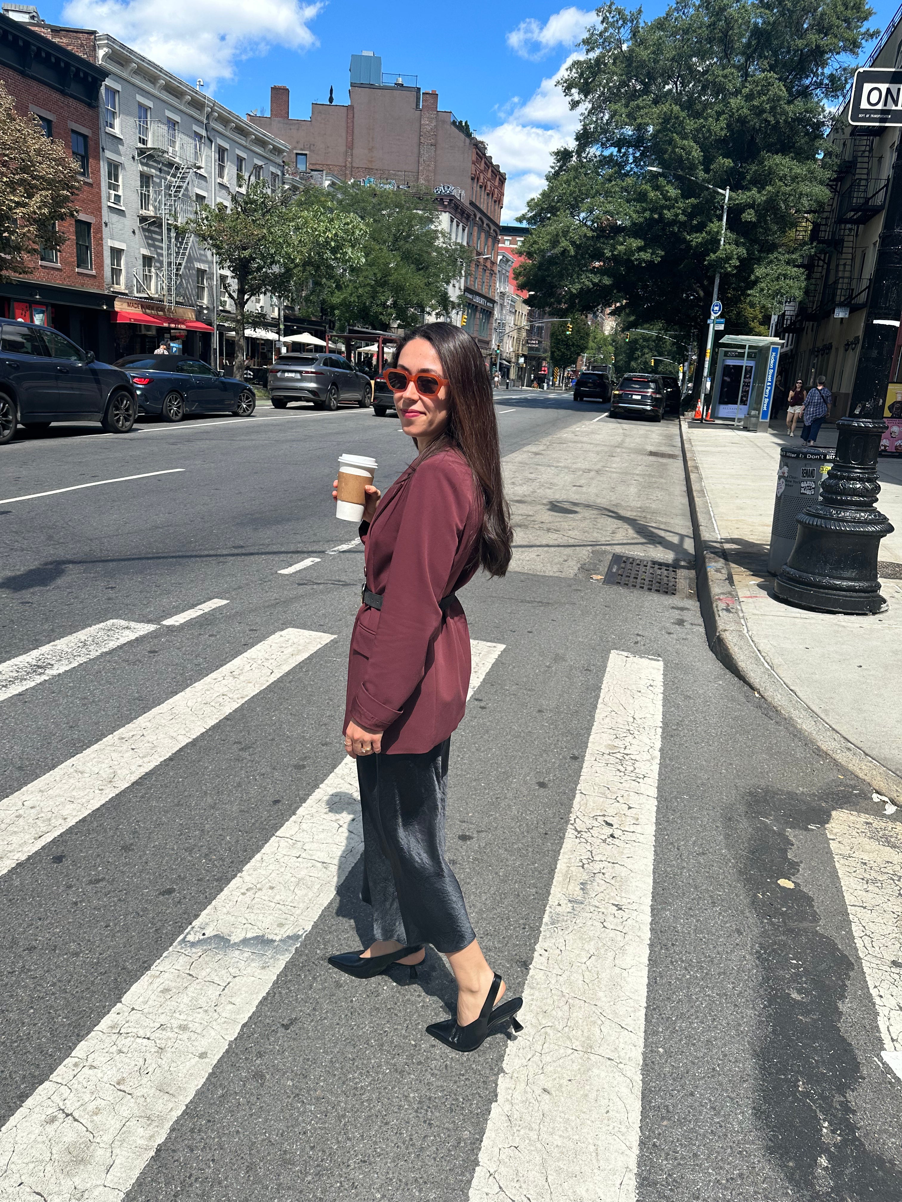 Woman standing on a city street corner holding a coffee cup wearing black slingbacks.