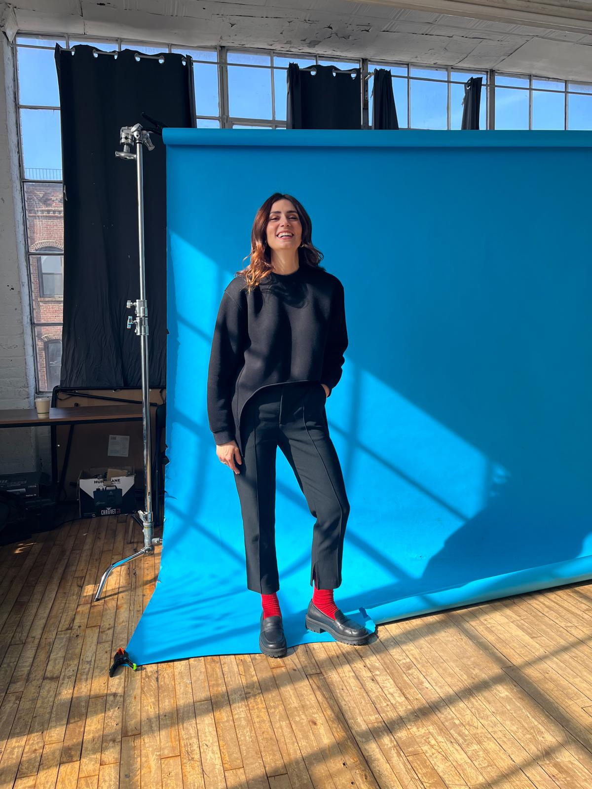 Person standing in front of a blue screen in a studio setting wearing black loafers