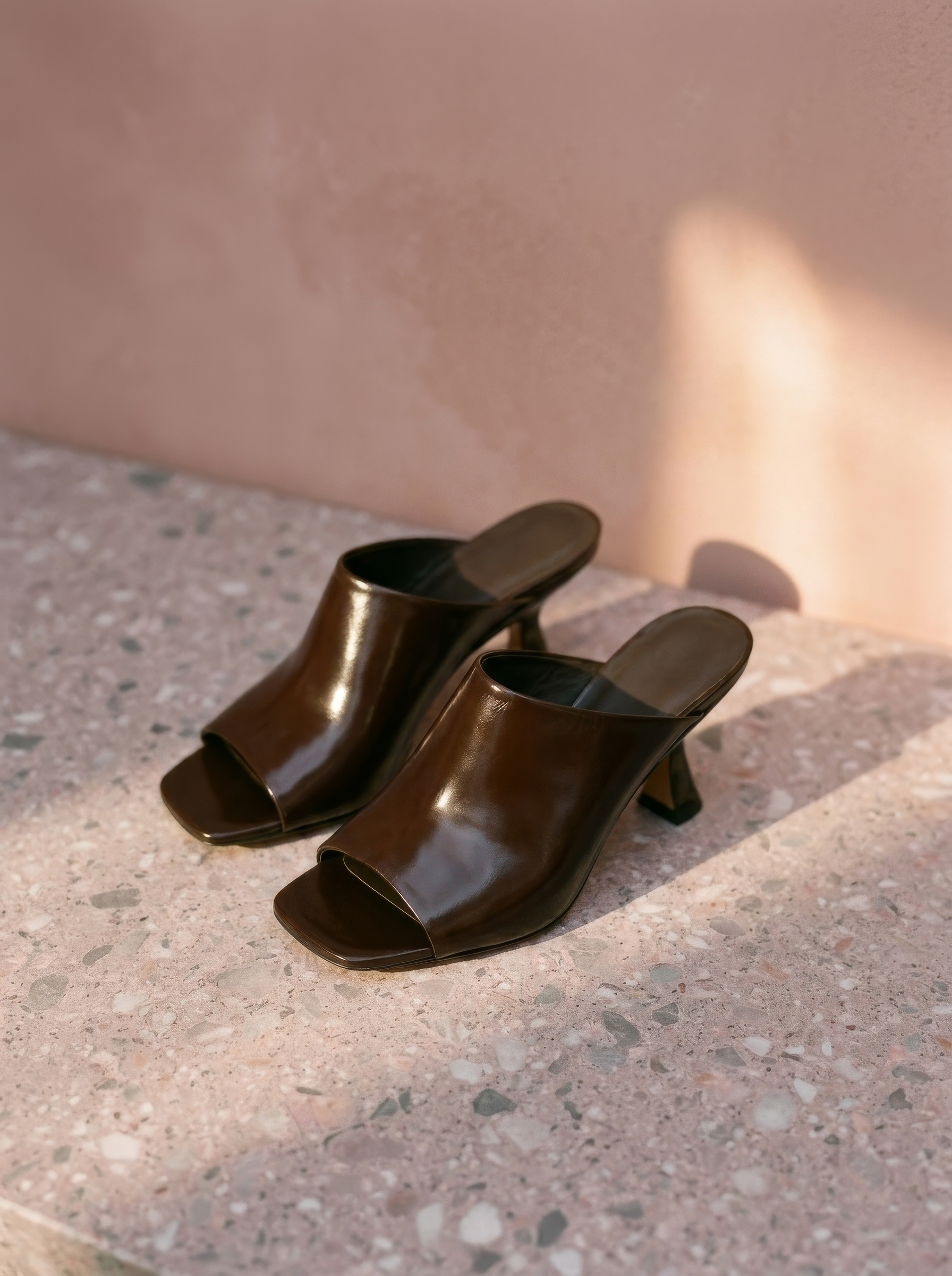 Pair of brown open-toe high-heeled shoes on a concrete surface with a neutral wall background.